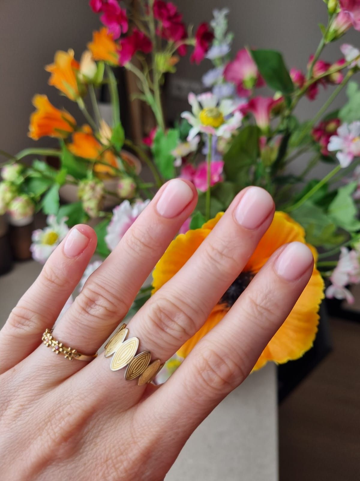 Zacht roze natuurlijke nagels met gouden ringen voor voorjaarsbloemen