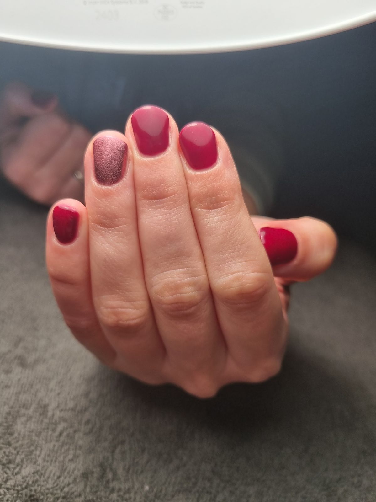 Donkerrode nagels met een fluweelachtig cateye-accent onder de lamp